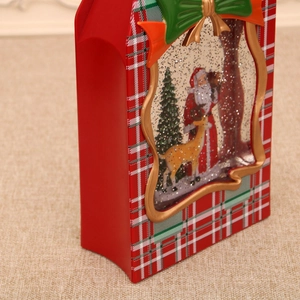Detail of red gift box snow globe with plaid pattern and a green festive bow decoration