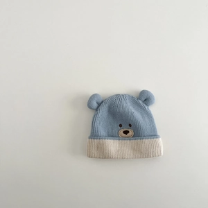 Detail of baby knit hat with blue and beige patchwork, bear ears, and cute embroidery