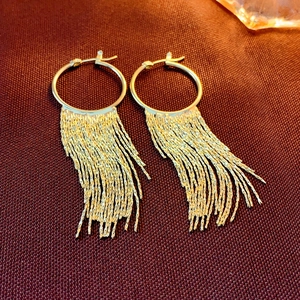 Detail of gold circle earrings with long textured chain tassels on a dark fabric
