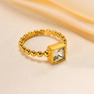 Macro shot of gold square zircon ring with beaded band over luxury champagne silk