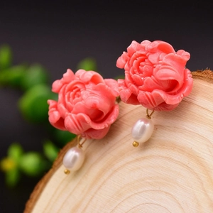 Macro shot of pink flower earrings with white pearl pendants on a textured wooden block