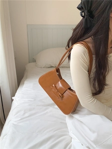 Detail of a brown glossy baguette bag with bow decoration worn by a model