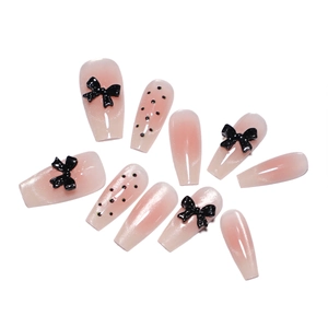 Pink gradient press-on nails featuring black bows, dots, and rhinestones in coffin shape