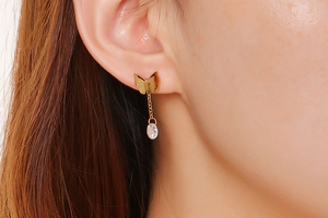 Nahaufnahme goldener Schmetterlings-Ohrring mit langer Kette und ovalem Edelstein an Model
