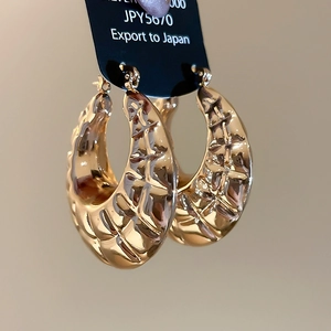 Close-up of golden chunky hoop earrings featuring a vintage textured diamond pattern