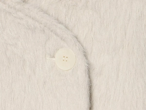 Macro view of plush faux fur texture and matching round button on cream casual coat