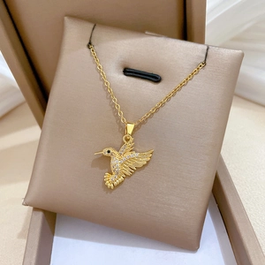 Detailed close-up of a gold hummingbird necklace with white zircons on a jewelry pillow