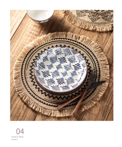Detail of round jute placemat with tassels and patterned ceramic plate on wooden table