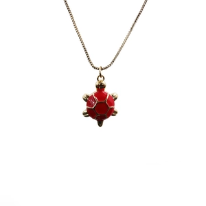Detail of a gold plated turtle pendant with vibrant red enamel on a delicate link chain