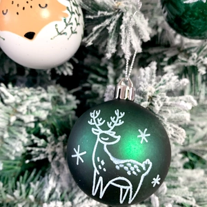 Detail of matte green and white Christmas balls with fox and deer patterns on a snowy tree