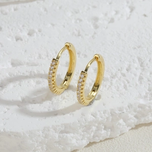 Macro shot of gold-plated hoop earrings with micro-pave white zircon on stone background