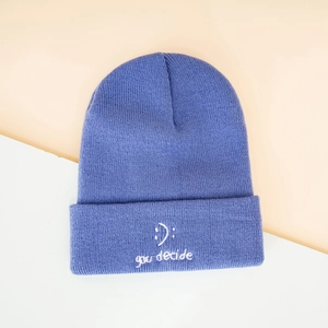 Close-up of blue knitted beanie with fine vertical ribs and white 'you decide' embroidery