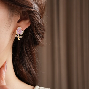 Detail of floral earring with purple petals and zircon leaves on a model