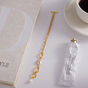Détail du bracelet doré à fermoir OT avec charme en émail floral et petite perle