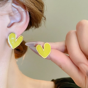Gros plan de boucles d'oreilles coeur en émail jaune vif avec bordures dorées sur l'oreille