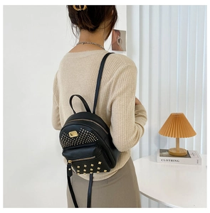 Detailed view of black leather mini backpack with gold rivets on a fashion model