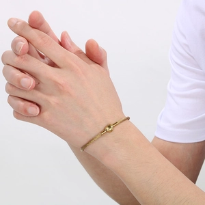 Detailed view of 3mm gold stainless steel wire bracelet with heart charm on female wrist