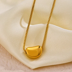 Minimalist gold bean pendant necklace with box chain on cream silk fabric