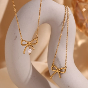 Close-up of golden bow-shaped pendant with a white pearl on a delicate metal chain