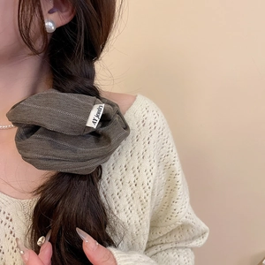 Detail of brown herringbone fabric scrunchie with brand label on braided hair