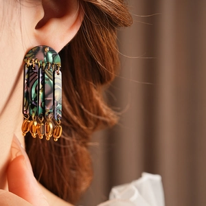 Detail of bohemian iridescent shell tassel earrings with gold beads on a model