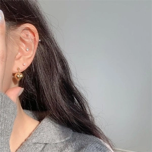 Macro view of gold-finished heart drop earrings with polished surface on a model