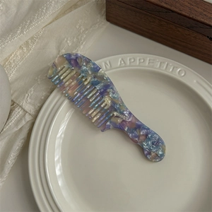 Macro shot of large acetate wide-tooth comb with colorful marble texture on a white plate