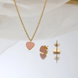Set di gioielli a cuore rosa con collana dorata e orecchini su seta bianca