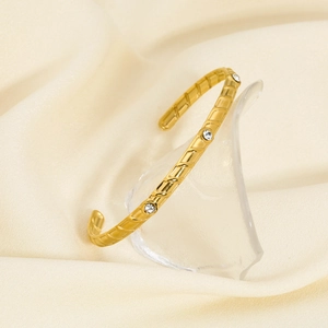 Detailed close-up of a gold-plated stainless steel cuff featuring diagonal grooves and zircons