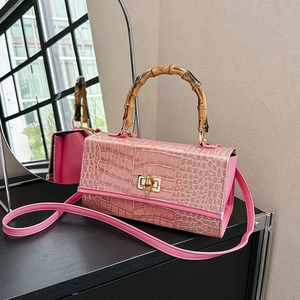 Detail of pink croc-embossed handbag featuring a vintage bamboo handle and gold twist lock