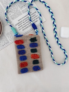 Plush crossbody phone bag with colorful 3D dots and woven strap on newspaper background
