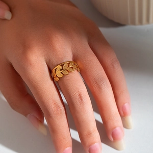 Close-up of golden leaf pattern titanium steel open ring worn on a model's finger