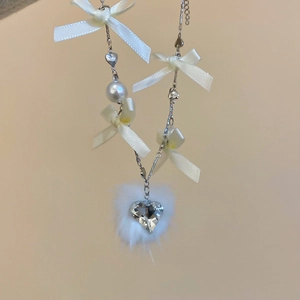Detail of ribbon bow necklace with pearl, heart crystal, and soft white pompom charm