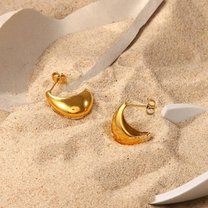 Detailed view of polished 18K gold plated chunky crescent hoop earrings on sand