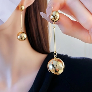Close-up of a model wearing golden metal ball tassel drop earrings in a minimalist style