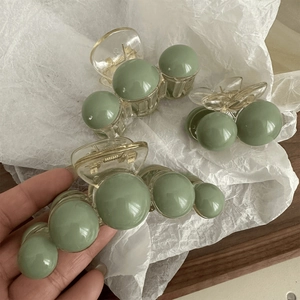 Detailed view of avocado green pearl hair claws in large and small sizes on a wooden plate