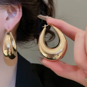 Detail of large glossy gold teardrop hoop earrings showing polished metallic finish