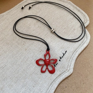 Macro detail of red five-petal flower pendant with heart carving on adjustable black cord