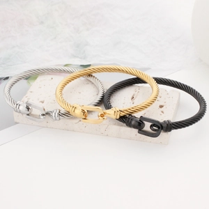 Three horseshoe buckle cable bangles in silver, gold, and black steel on a stone pedestal
