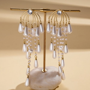 Detail shot of elegant gold tassel earrings with teardrop pearls on a display stand
