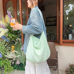 Détail d'un sac cabas à carreaux vert clair porté par un mannequin en décor estival