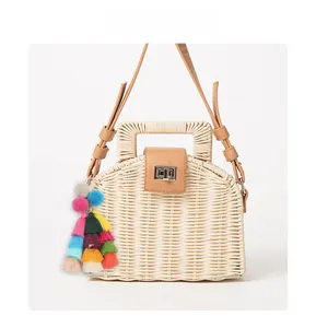 Detail of colorful tassel and pom-pom charms on a woven straw handbag with a metal lock