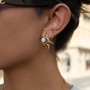 Two-tone sunburst stud earrings with pearl center worn by a model in outdoor setting