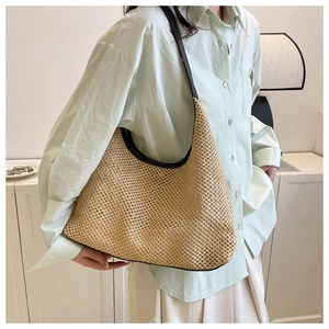 Detail of khaki woven straw tote bag featuring intricate openwork texture and black straps