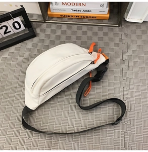 Top view of beige waterproof crossbody bag with orange drawstrings on grey mesh mat