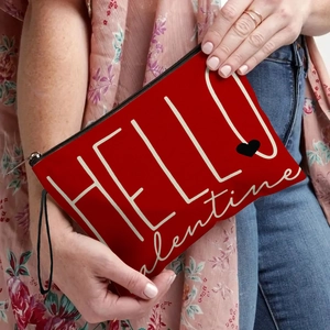 Red canvas makeup bag with 'HELLO Valentine' print held by a model in floral outfit
