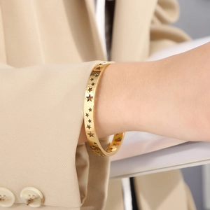 Detailed view of hollow star bangle in 18K gold finish worn on a model wrist