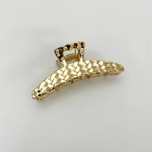 Macro detail of golden woven texture metal hair claw clip on white background