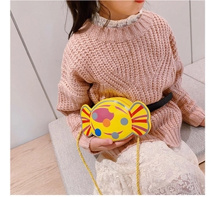 Gros plan d'un sac bandoulière jaune en forme de bonbon porté par un enfant en rose