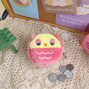 Close-up of a plush pink owl coin purse with embroidery details on a white lace background
